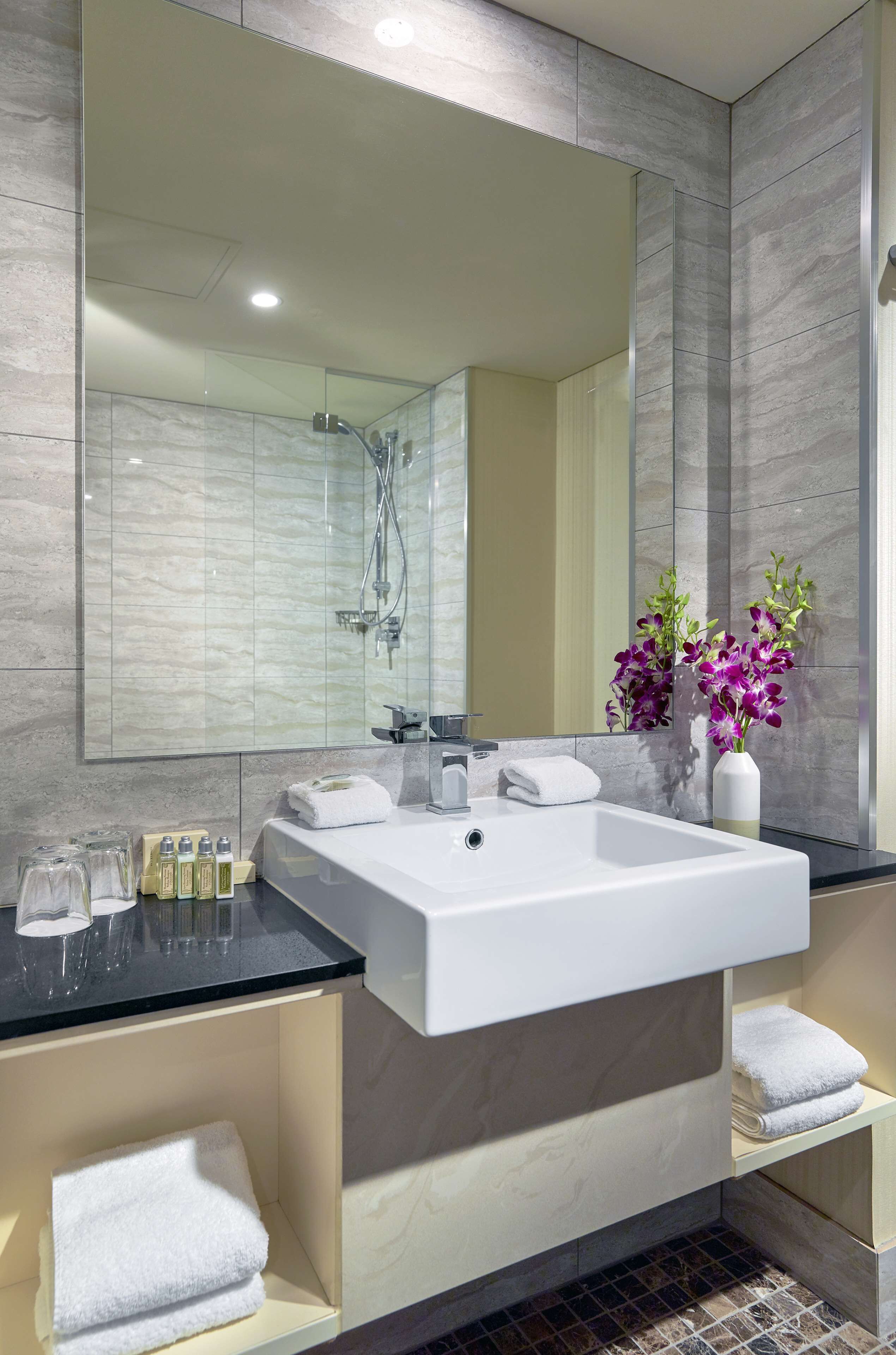 A modern bathroom with a large mirror, a white sink, and a shower.