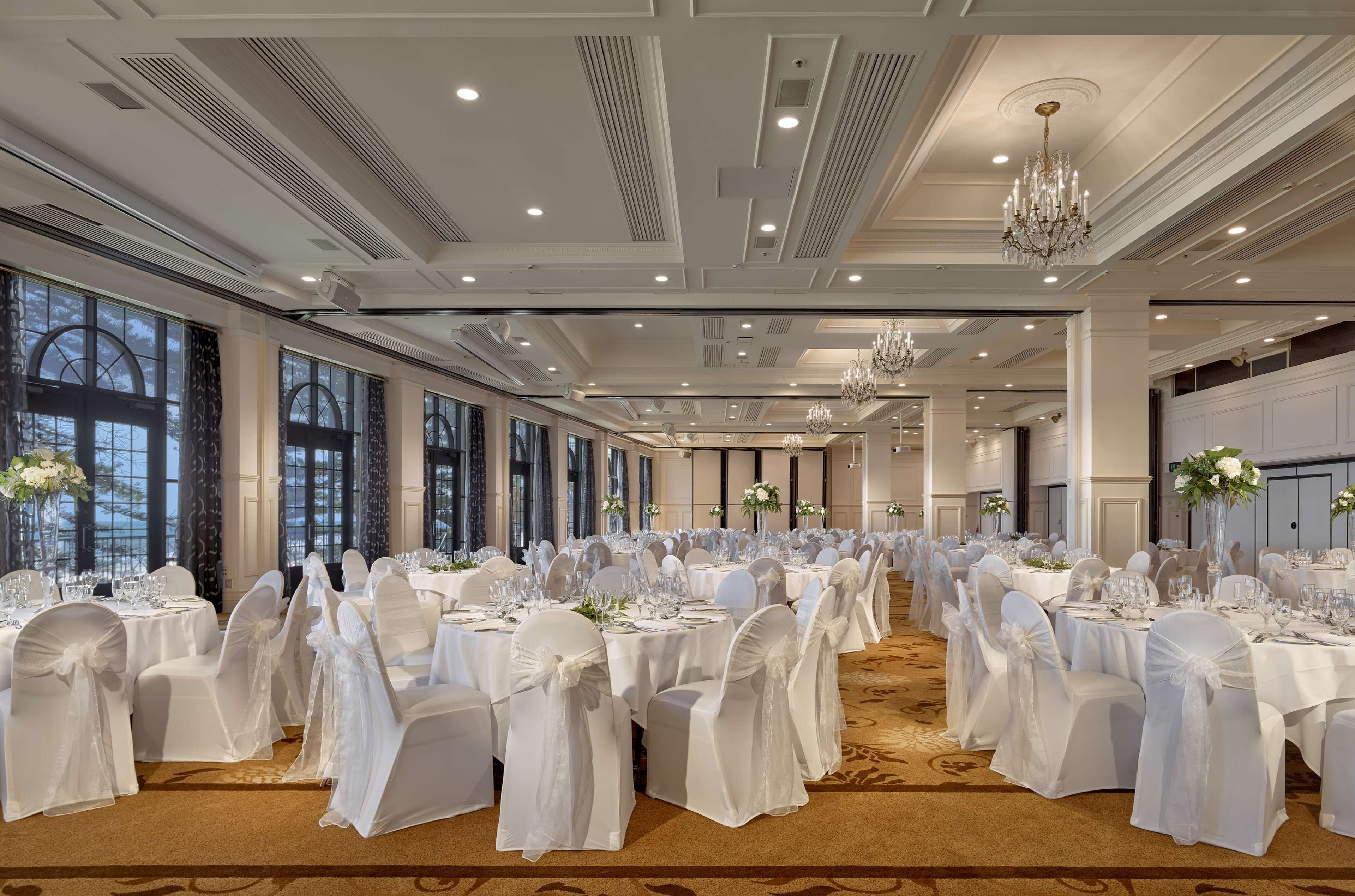 Een feestzaal met ronde tafels, witte tafelkleden en stoelen versierd met witte linten.