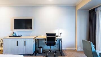 A hotel room with a bed, a desk with a chair, a TV, and a window with curtains.