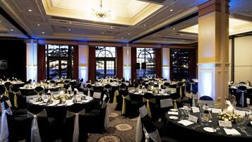 A banquet hall with round tables, black and white chairs, chandeliers, and large windows.
