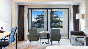 Una habitación de hotel con balcón, un escritorio con silla, un sofá y una lámpara.