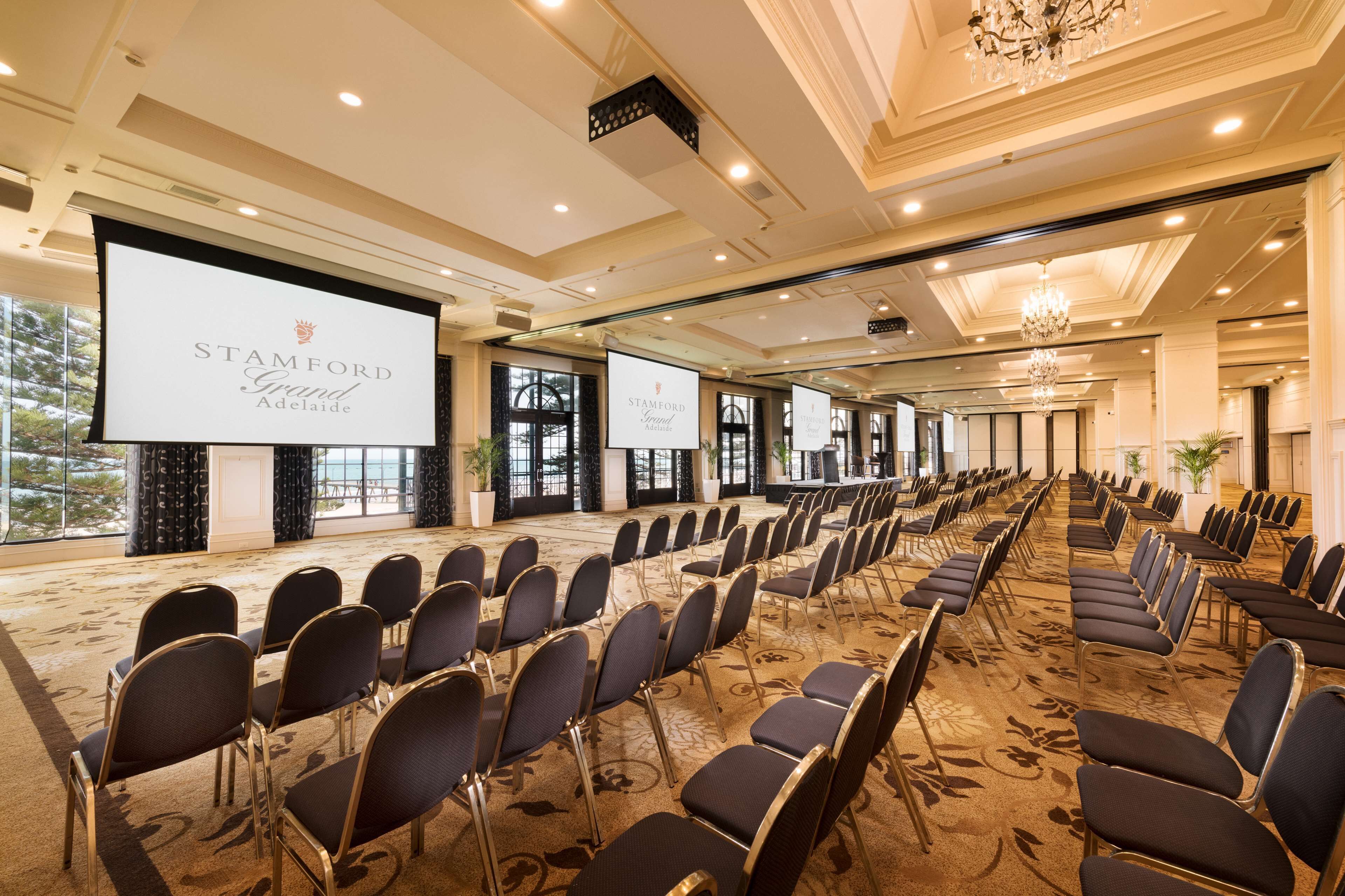 A conference room with rows of chairs, a large screen, and a chandelier.