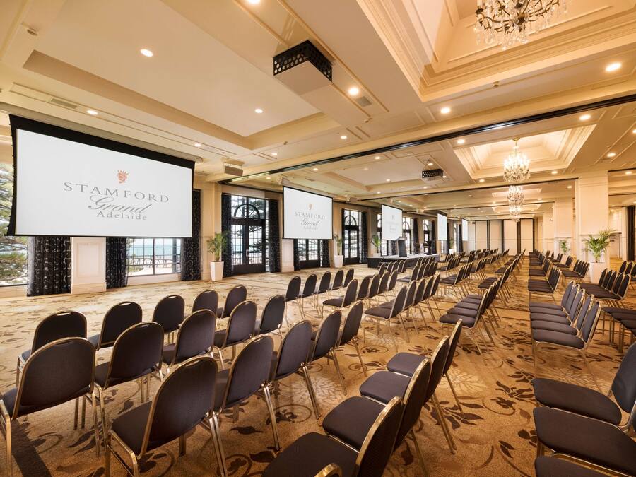 A conference room with rows of chairs, a large screen, and a chandelier.