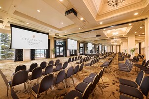 Un salón de conferencias con hileras de sillas, una pantalla grande y un candelabro.