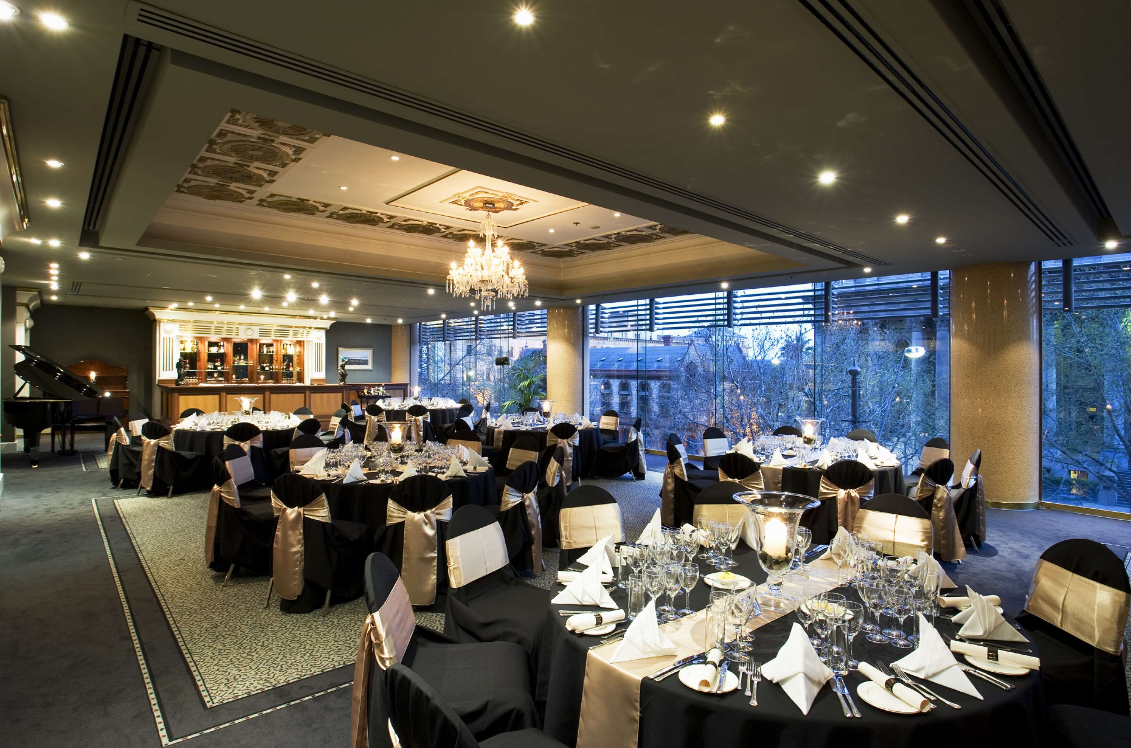 A banquet hall with round tables, chandeliers, and a piano.
