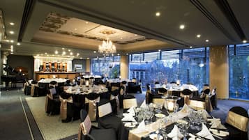 A banquet hall with round tables, chandeliers, and a piano.