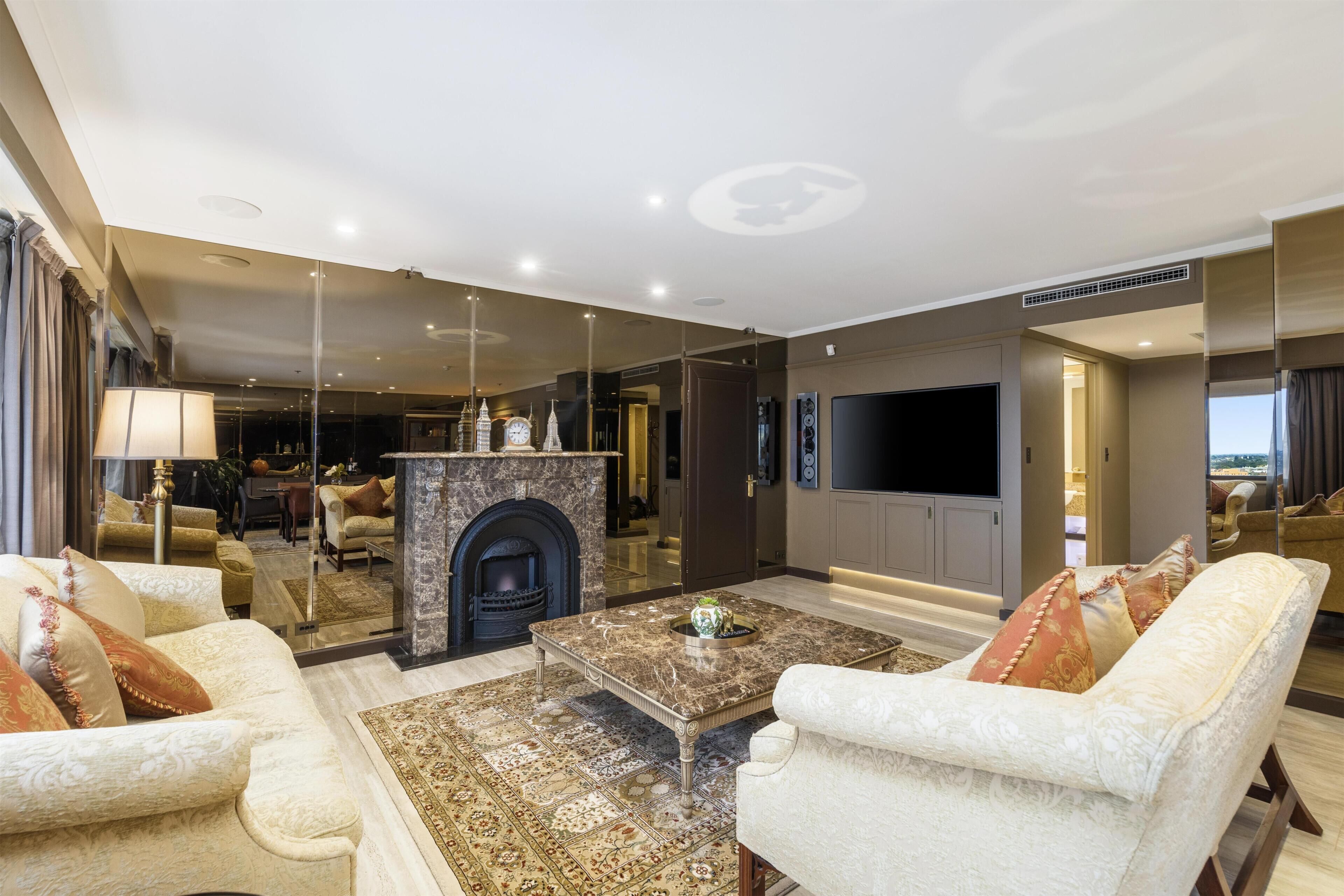 A spacious living room with a fireplace, comfortable seating, a flat-screen TV, and a large mirror reflecting the room.