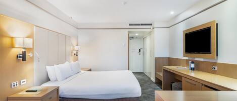A hotel room with a bed, bedside tables, a desk, a flat-screen TV, and a wardrobe.