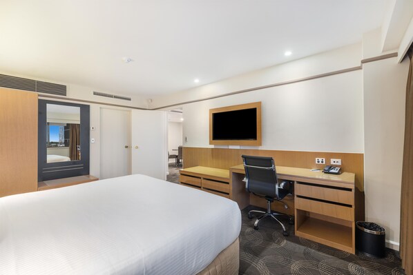 A hotel room with a bed, desk, chair, TV, and a trash bin.