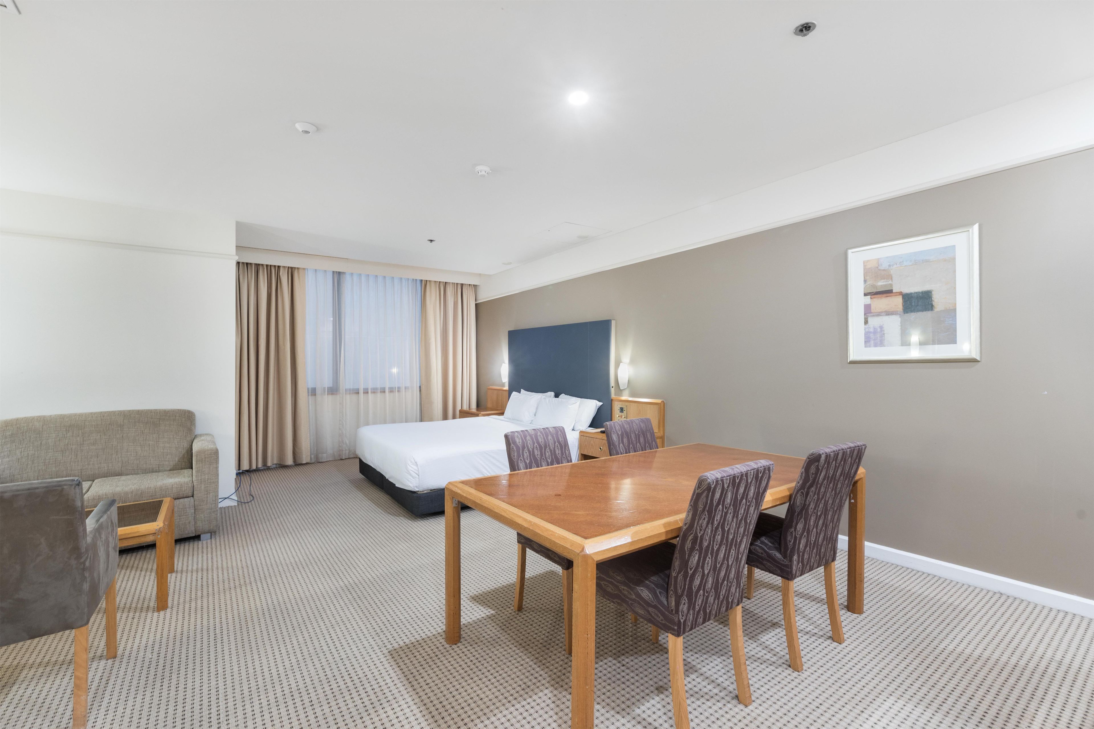 A hotel room with a bed, a desk, a chair, and a dining table.