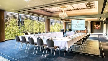A conference room with a long table, chairs, a chandelier, and a projection screen displaying 'STAMFORD Plaza Adelaide'.