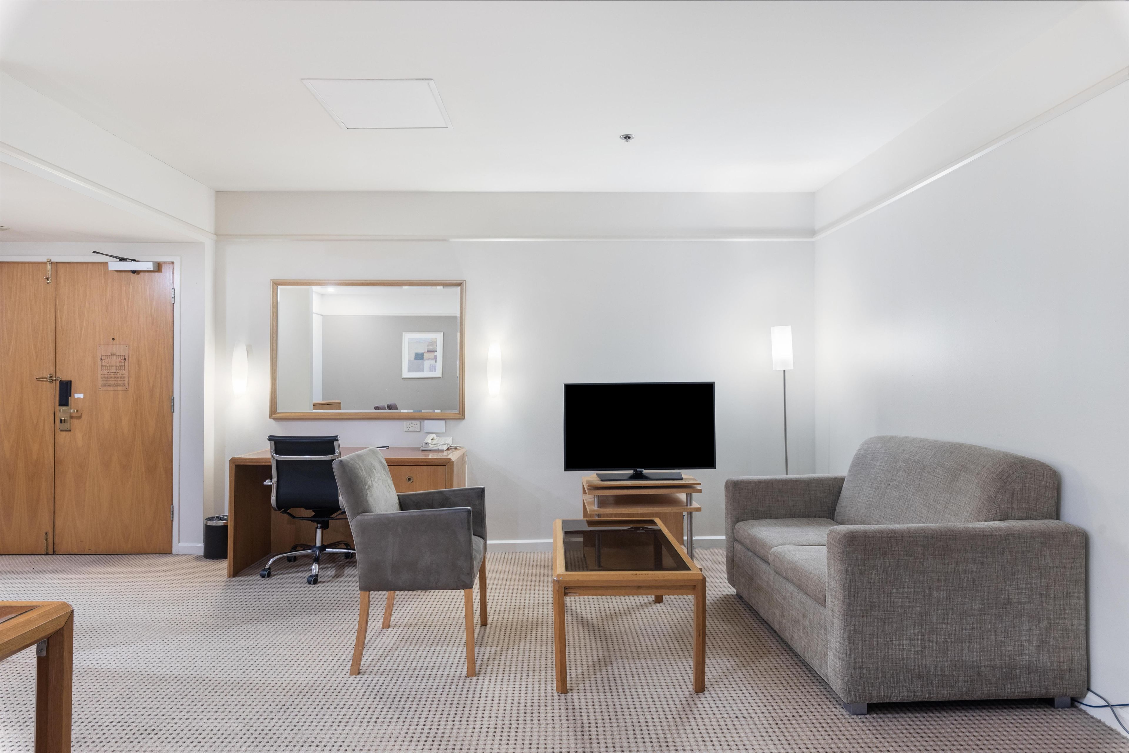 Une chambre d’hôtel équipée d’un bureau, d’une chaise, d’une télévision, d’un canapé et d’un miroir.