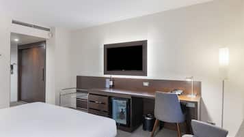 A hotel room with a bed, a desk with a television, a mini-fridge, a chair, and a lamp.