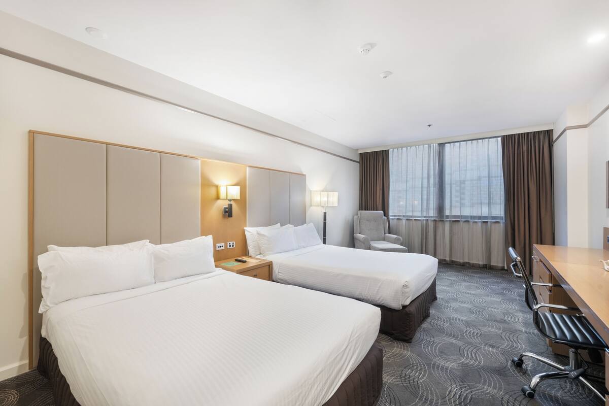 A hotel room with two beds, a desk, a chair, and a large window with curtains.