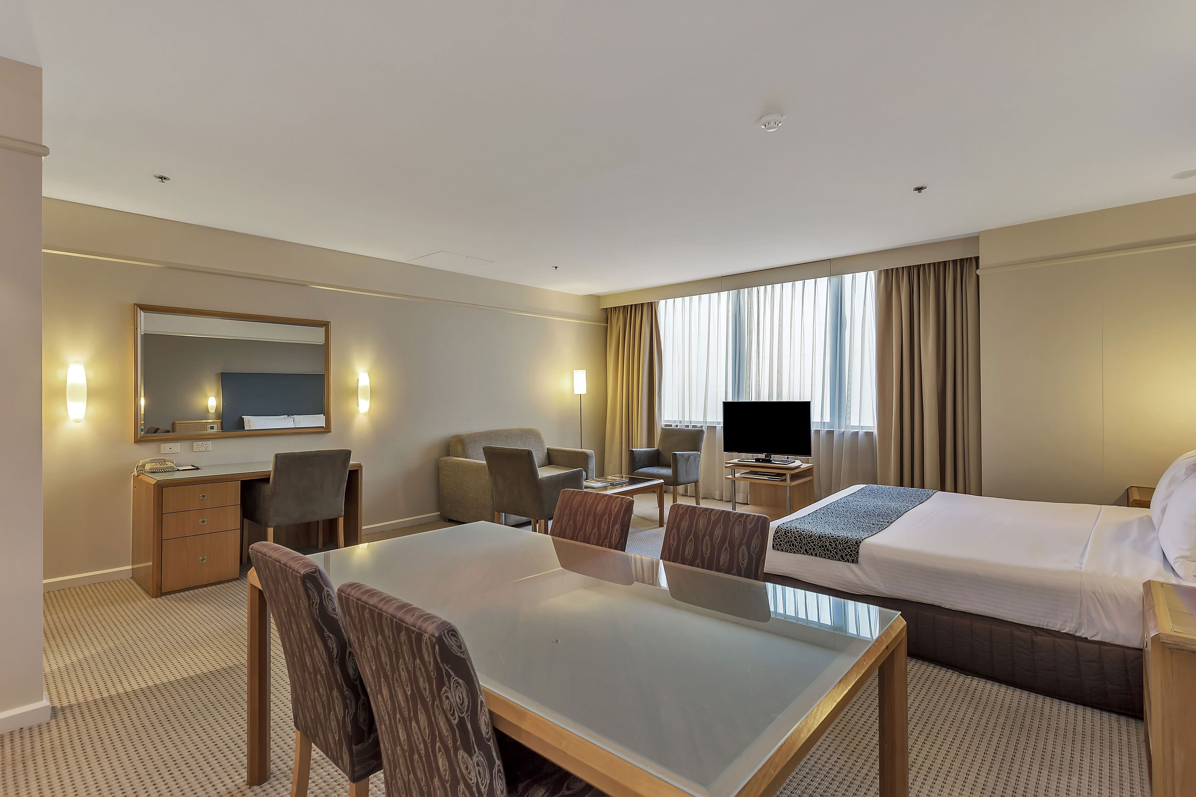 Une chambre d’hôtel équipée d’un lit, d’un bureau, de chaises, d’une télévision et d’une grande fenêtre avec des rideaux.