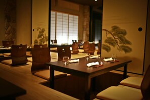 A restaurant with wooden tables and chairs, a traditional Japanese-style interior, and a view of the outside through large windows.