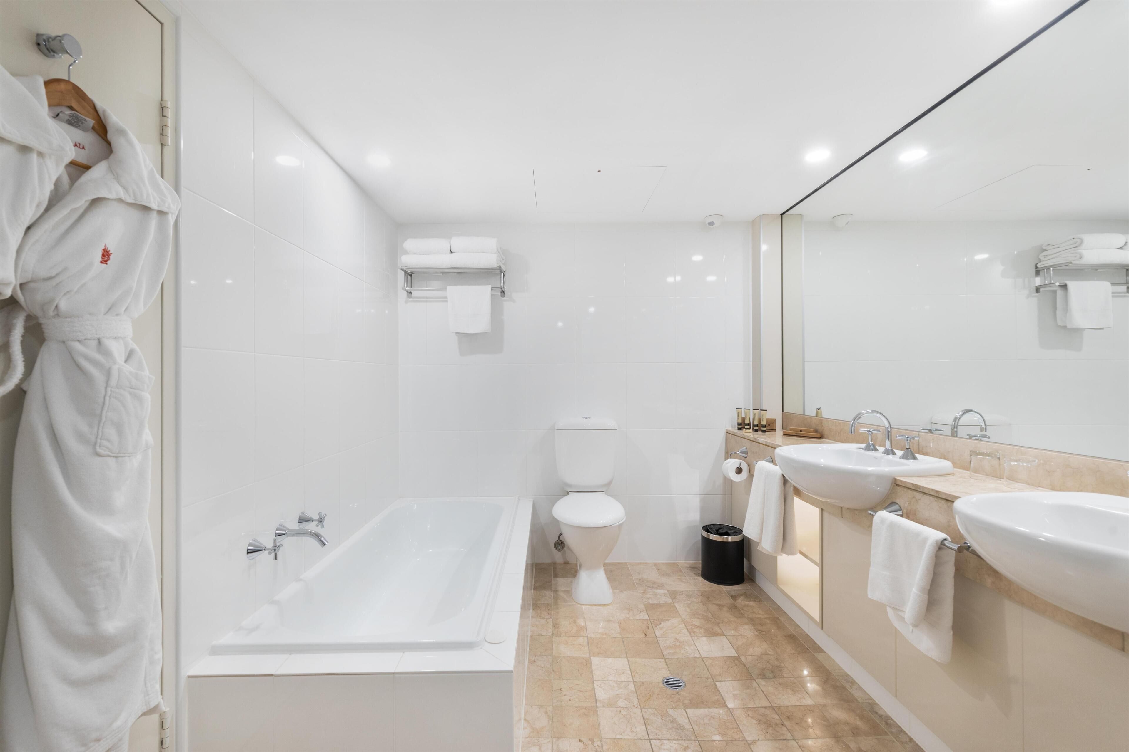 A modern bathroom with a bathtub, toilet, and two sinks.