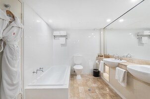 A modern bathroom with a bathtub, toilet, and two sinks.