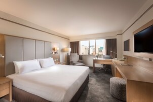 Habitación de hotel con una cama grande, un escritorio, una silla, un televisor y una ventana con vistas a la ciudad.