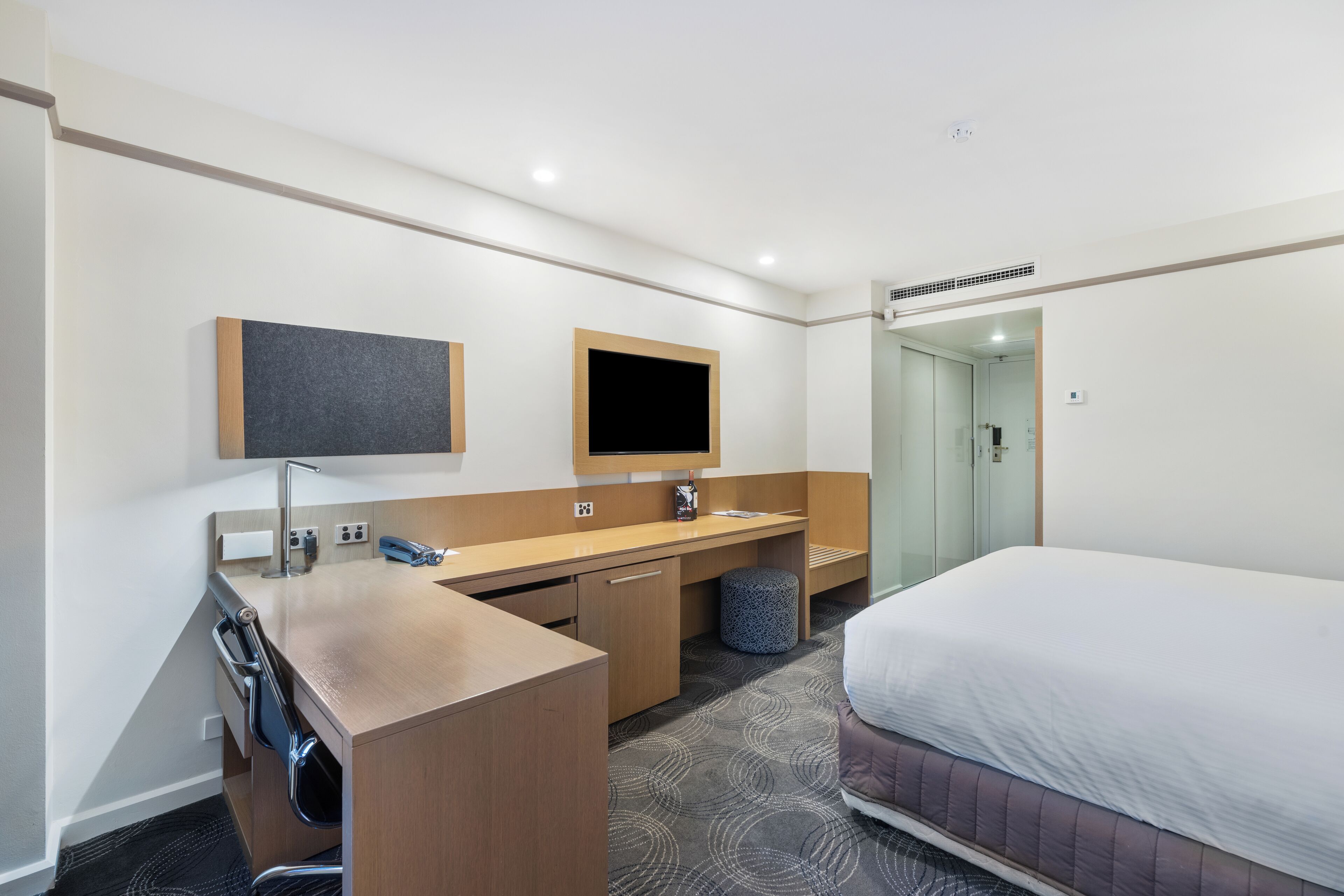 A hotel room with a bed, a desk with a chair, a sink, and a television.