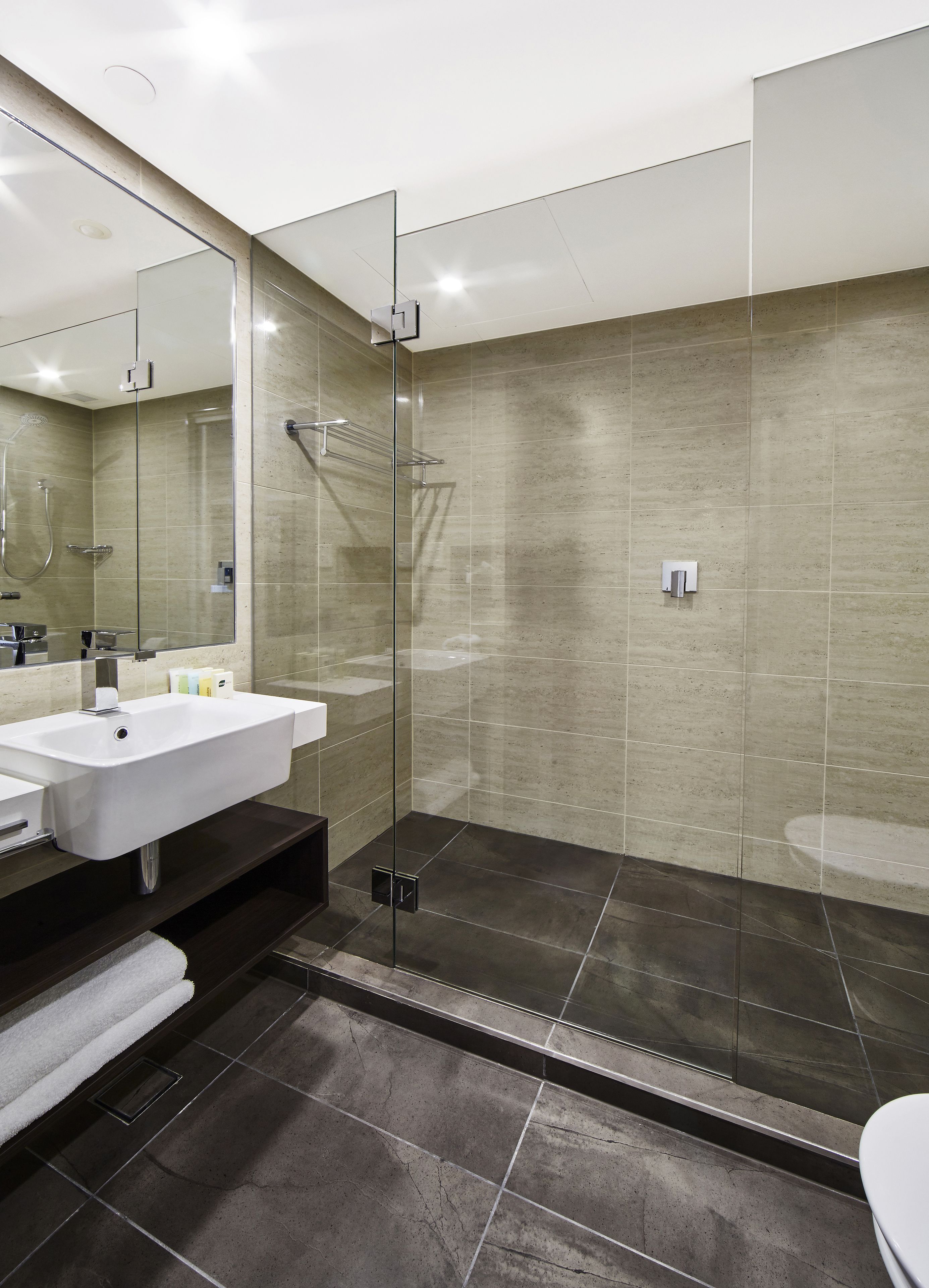 A modern bathroom with a glass-enclosed shower, a white sink, and a dark floor.