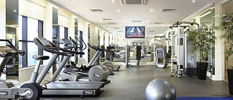 Un gimnasio con cintas de correr, elípticas, máquinas de pesas y una pelota grande de ejercicio.