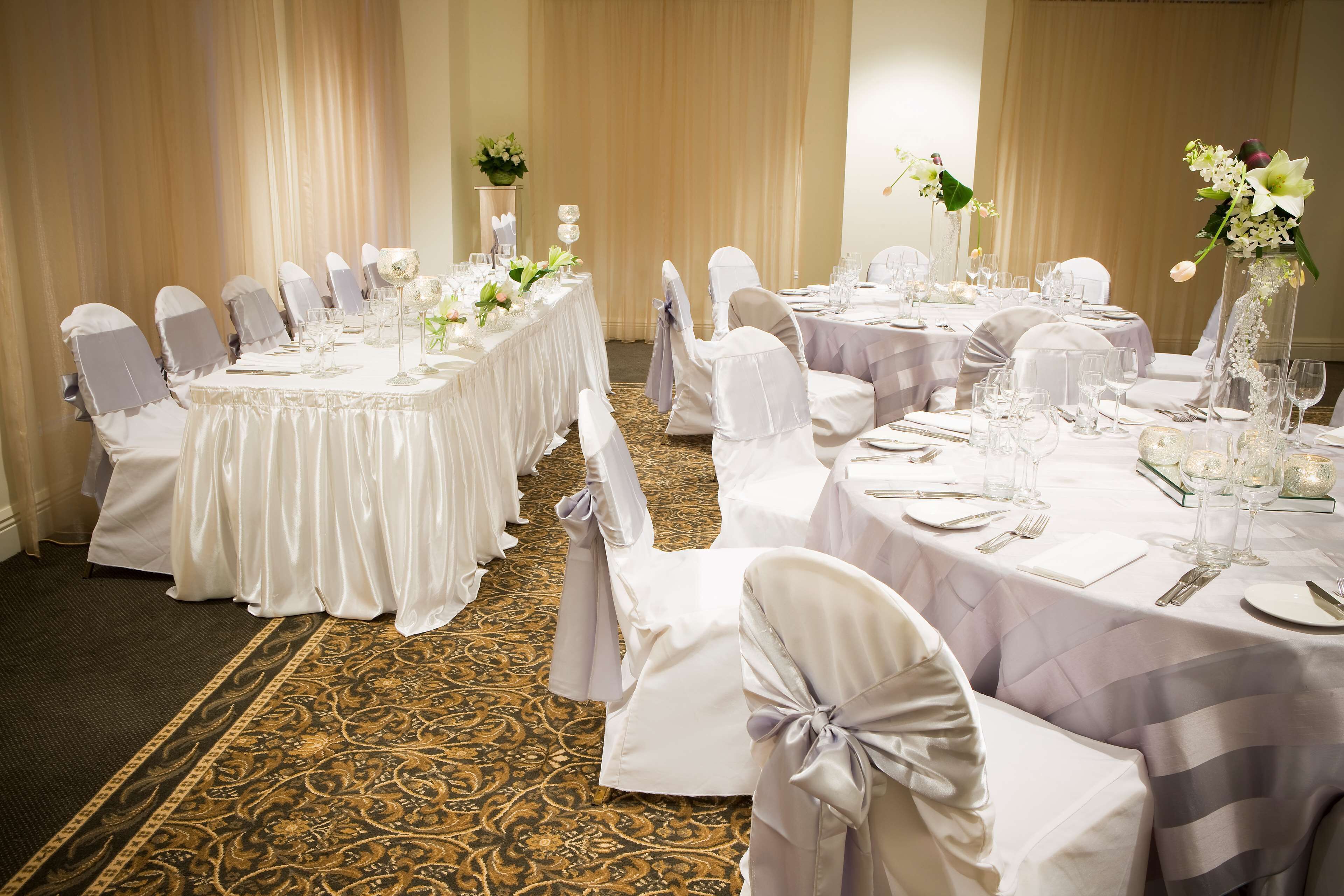 A banquet hall with round tables, white tablecloths, and chairs with bows.