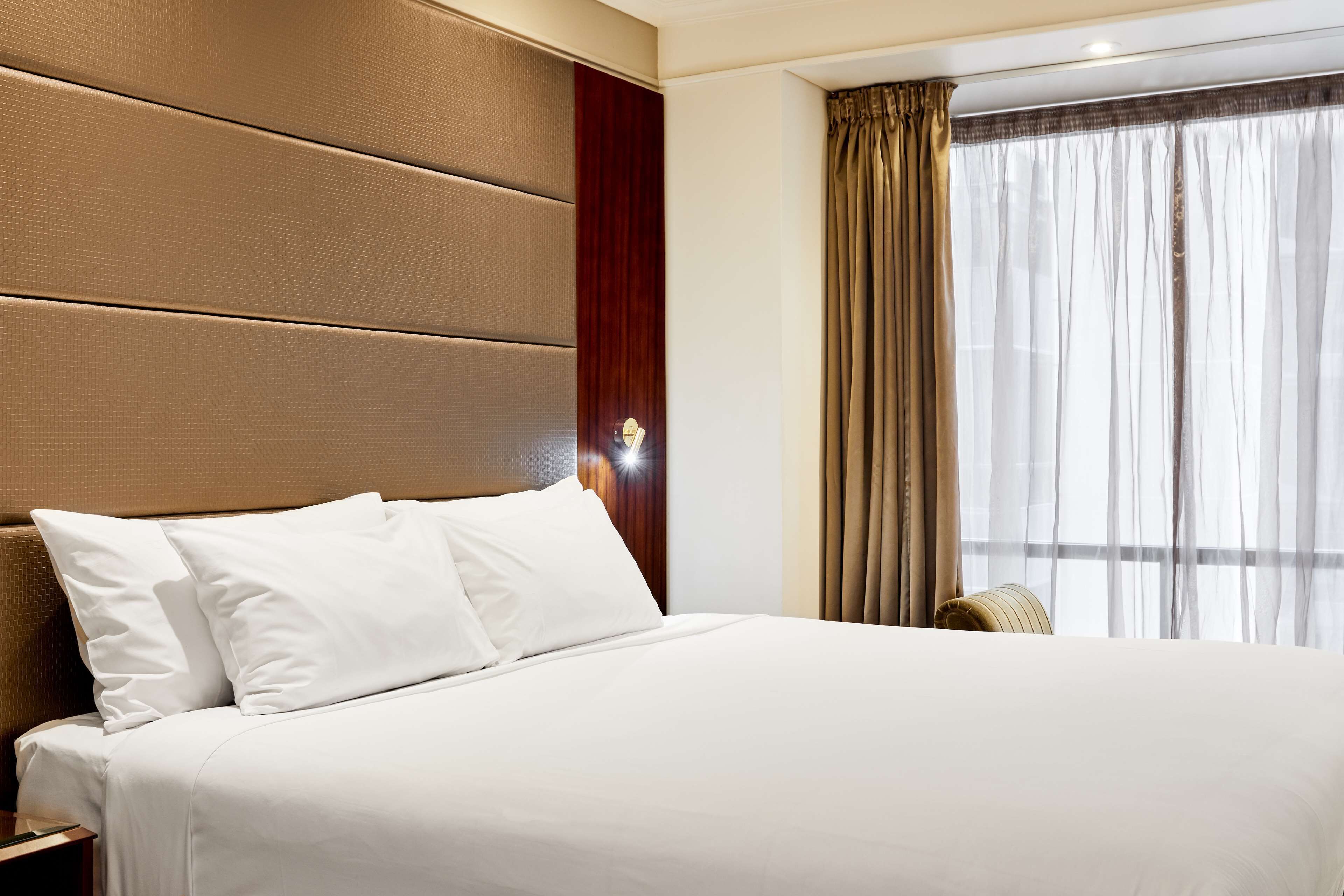 Une chambre d’hôtel avec un grand lit, une tête de lit en bois et une fenêtre avec des rideaux.