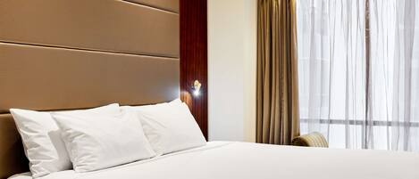 Une chambre d’hôtel avec un grand lit, une tête de lit en bois et une fenêtre avec des rideaux.