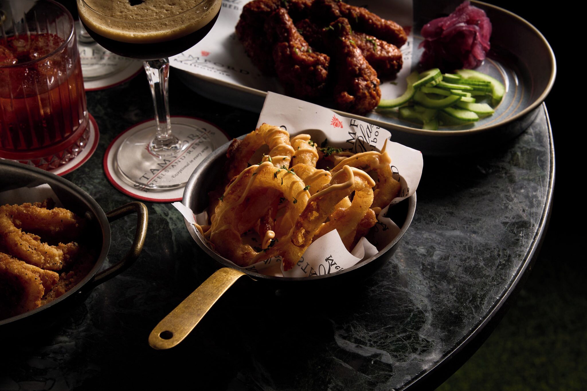 A table with a variety of dishes including fried chicken, a glass of red beverage, and a bowl of sliced cucumbers.