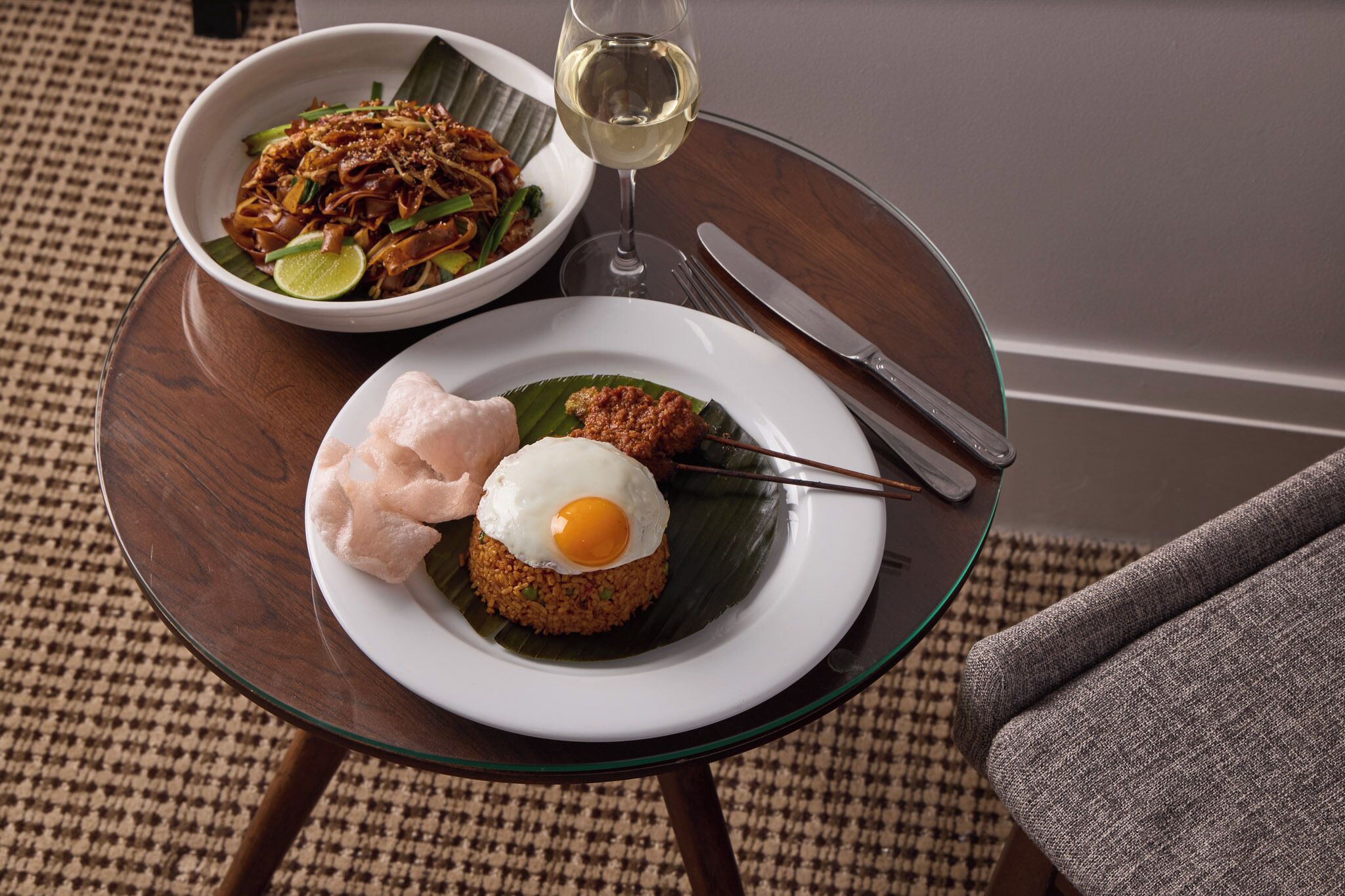 A table with two dishes, a glass of white wine, and cutlery.