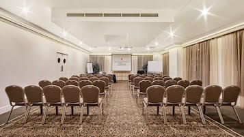 A conference room with rows of chairs, a projector screen, and a carpeted floor.