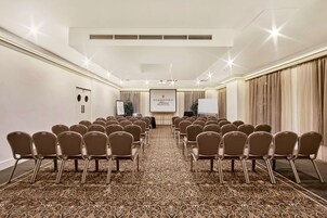 A conference room with rows of chairs, a projector screen, and a carpeted floor.