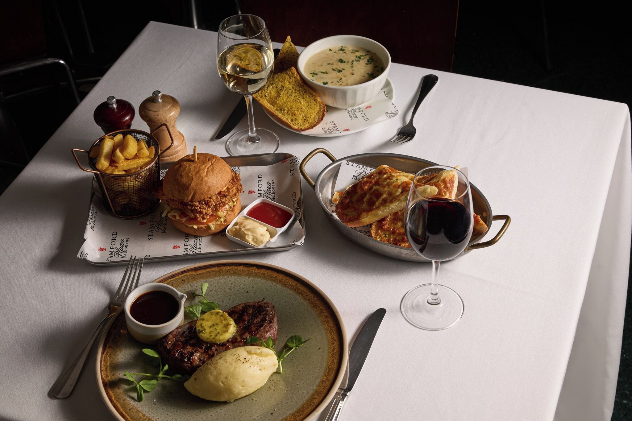 A table set with various dishes including steak, mashed potatoes, and bread, along with wine glasses and condiments.