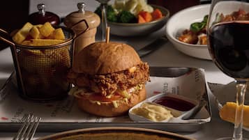 A meal with a fried chicken sandwich, fries, and a glass of red wine on a table.