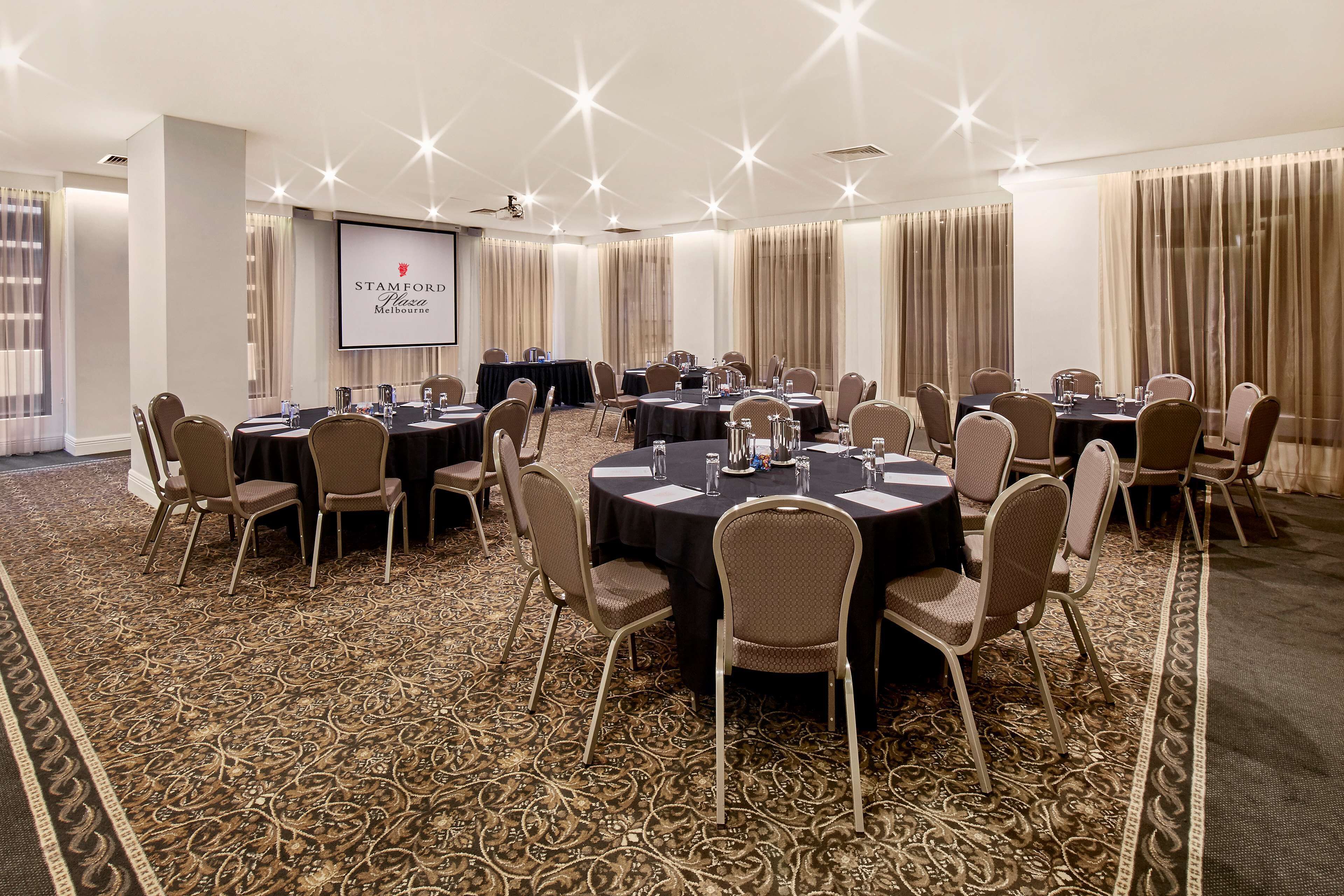 A conference room with round tables, chairs, a projector screen, and a carpeted floor.
