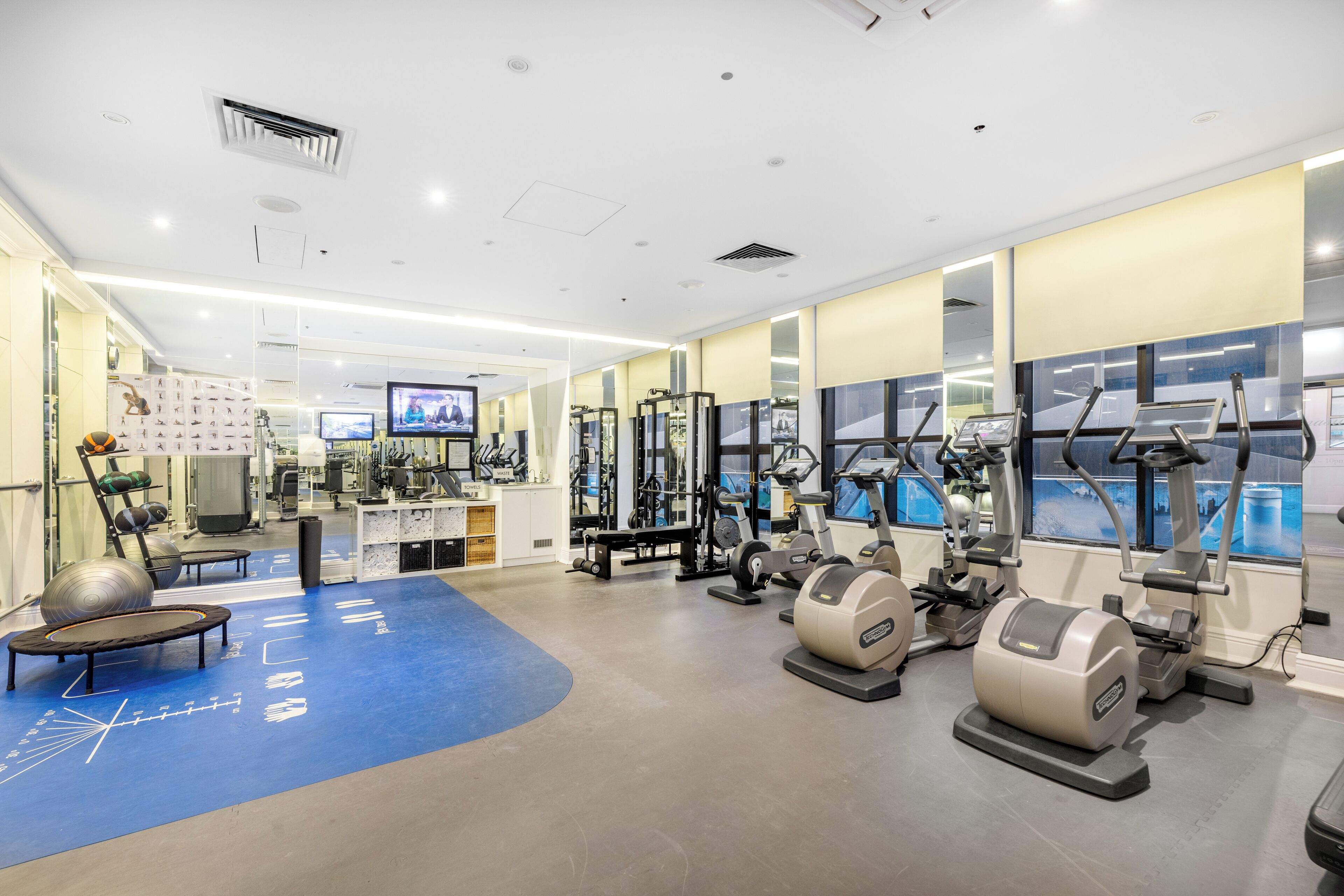 A modern gym with various exercise equipment, a blue mat area, and a large window providing a view.