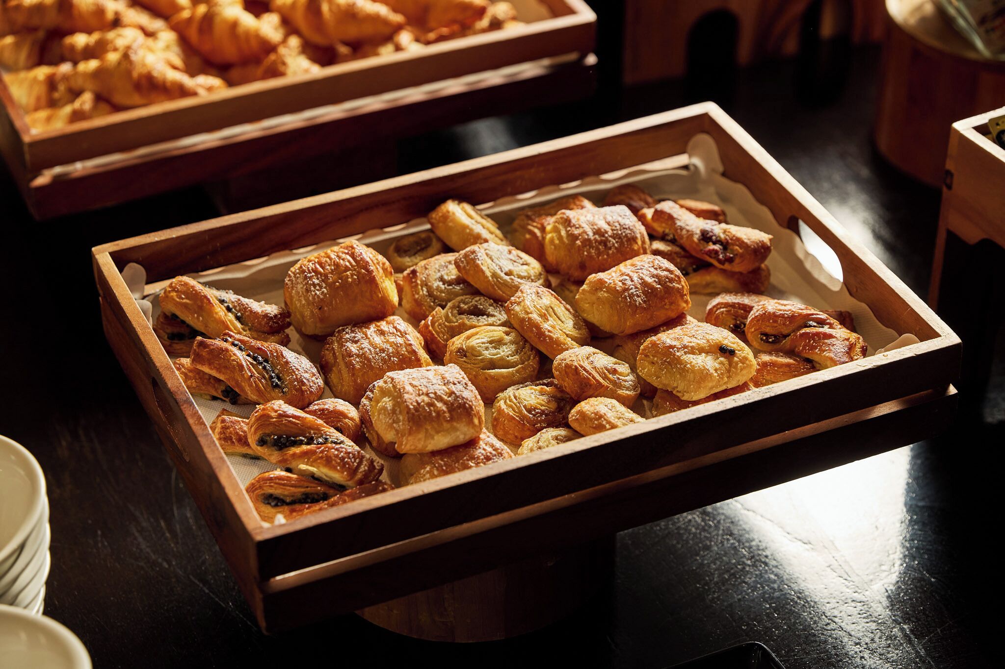 A wooden tray filled with various pastries, including croissants and puff pastries, displayed on a table.