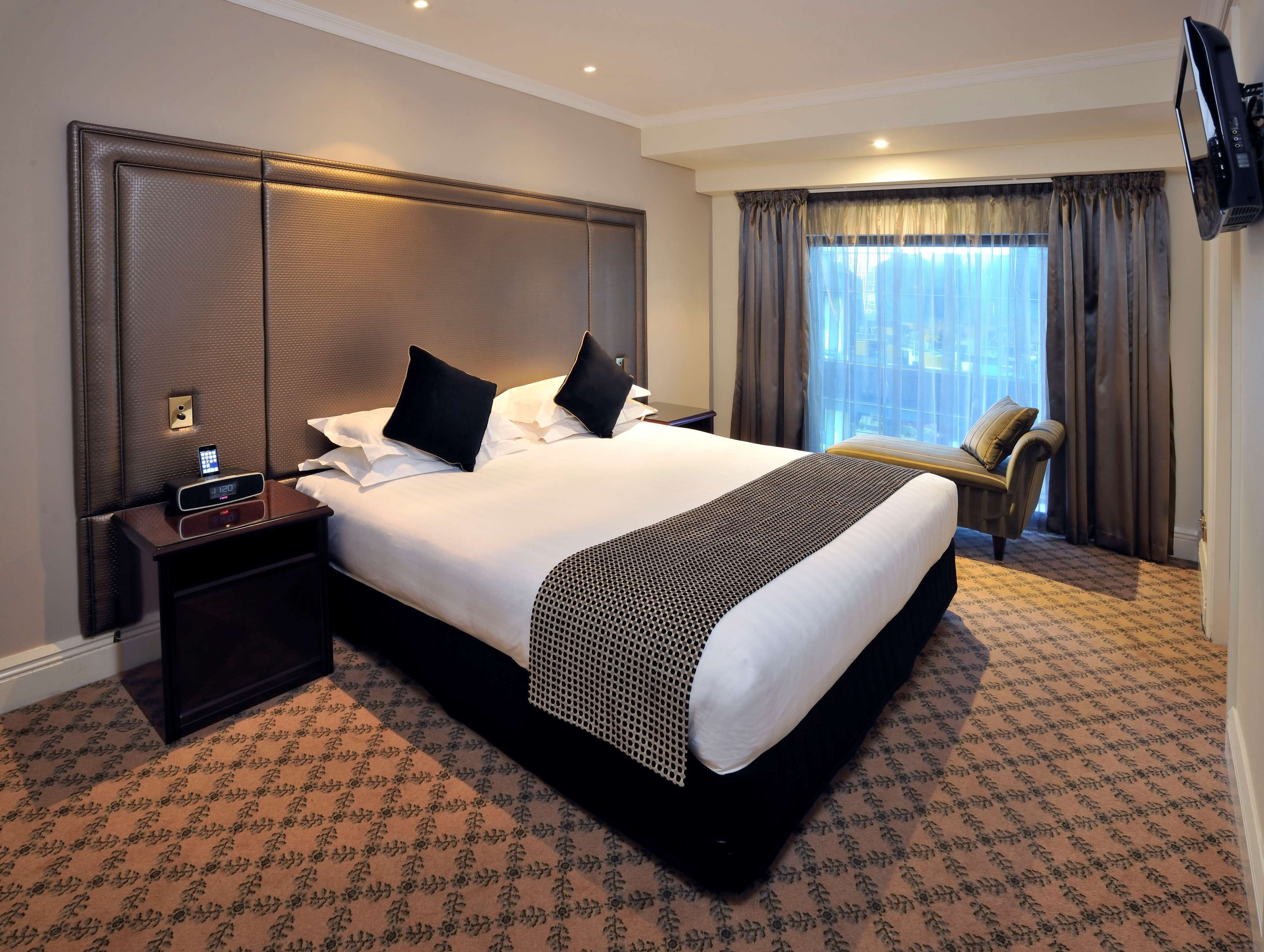 A hotel room with a large bed, a nightstand, a TV, and a window with curtains.