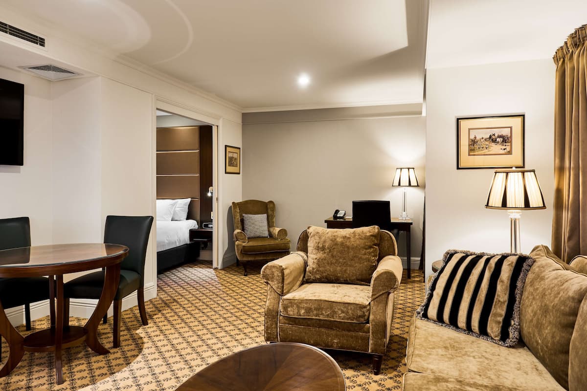 Une chambre d’hôtel comprenant un lit, un coin salon avec un canapé et un fauteuil, une table à manger et une lampe.