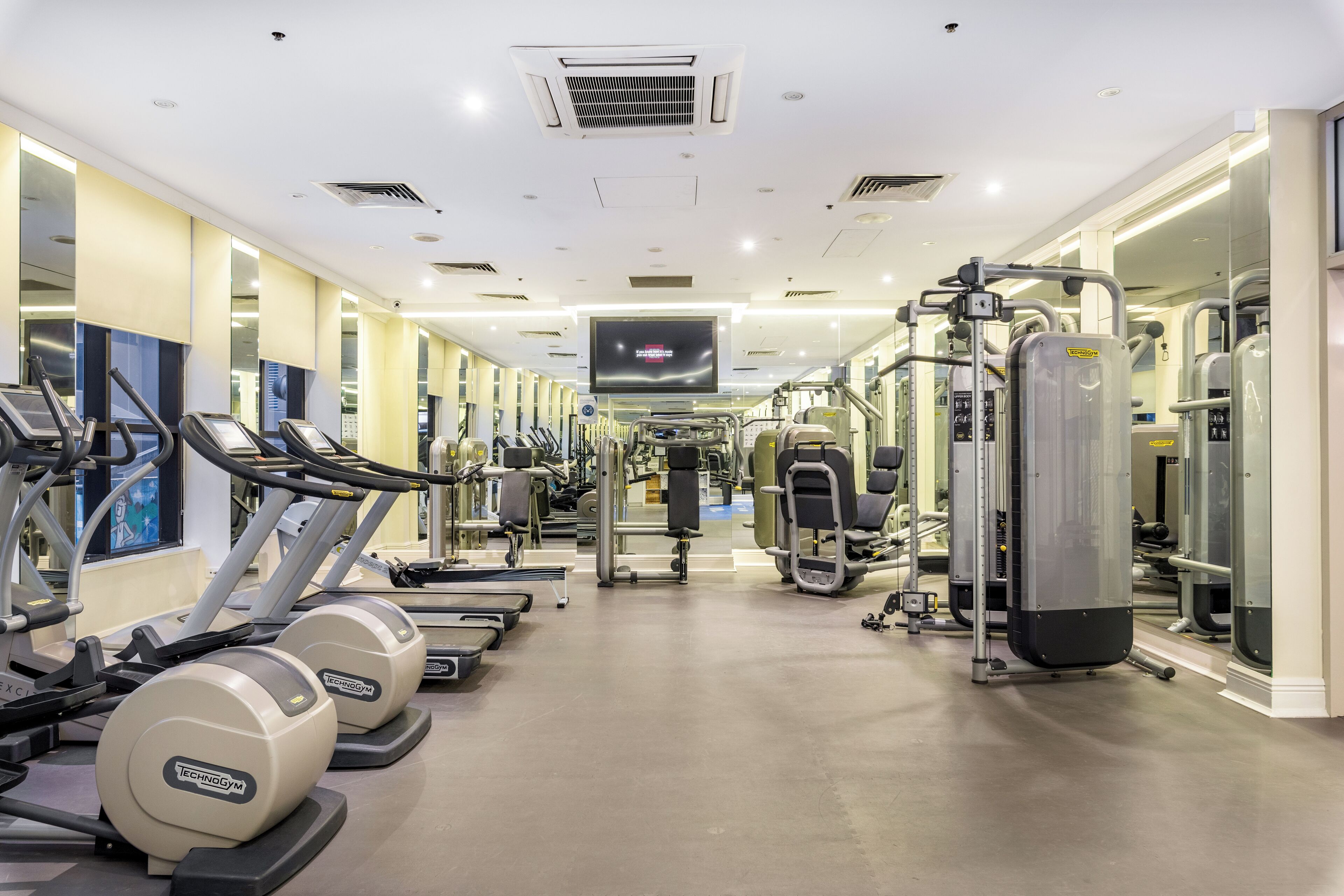 Ein Fitnessstudio mit Laufbändern, Kraftgeräten und einem Fernsehbildschirm.