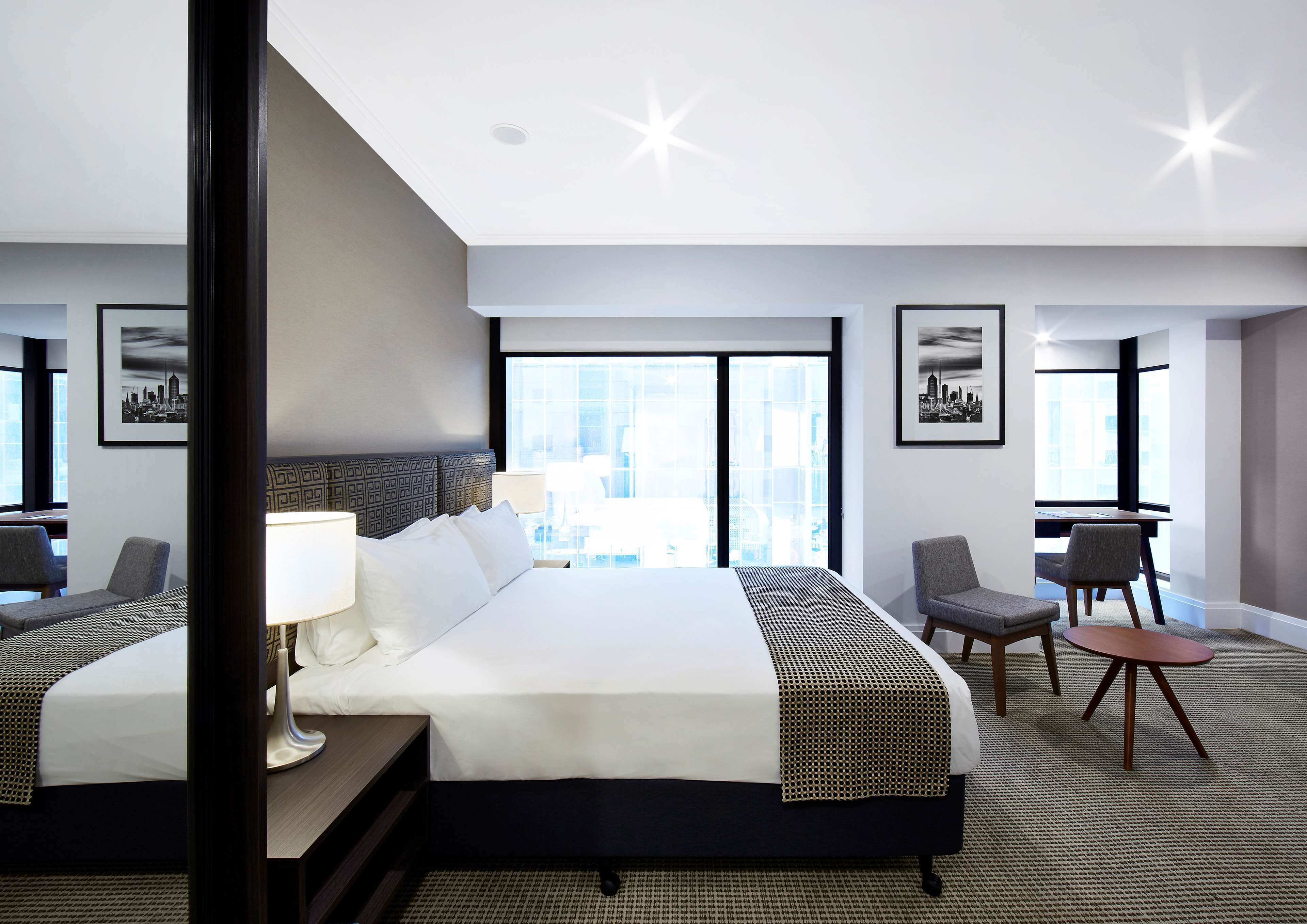 Ein Hotelzimmer mit einem großen Bett, zwei Sesseln, einem kleinen Tisch und Blick auf die Stadt.
