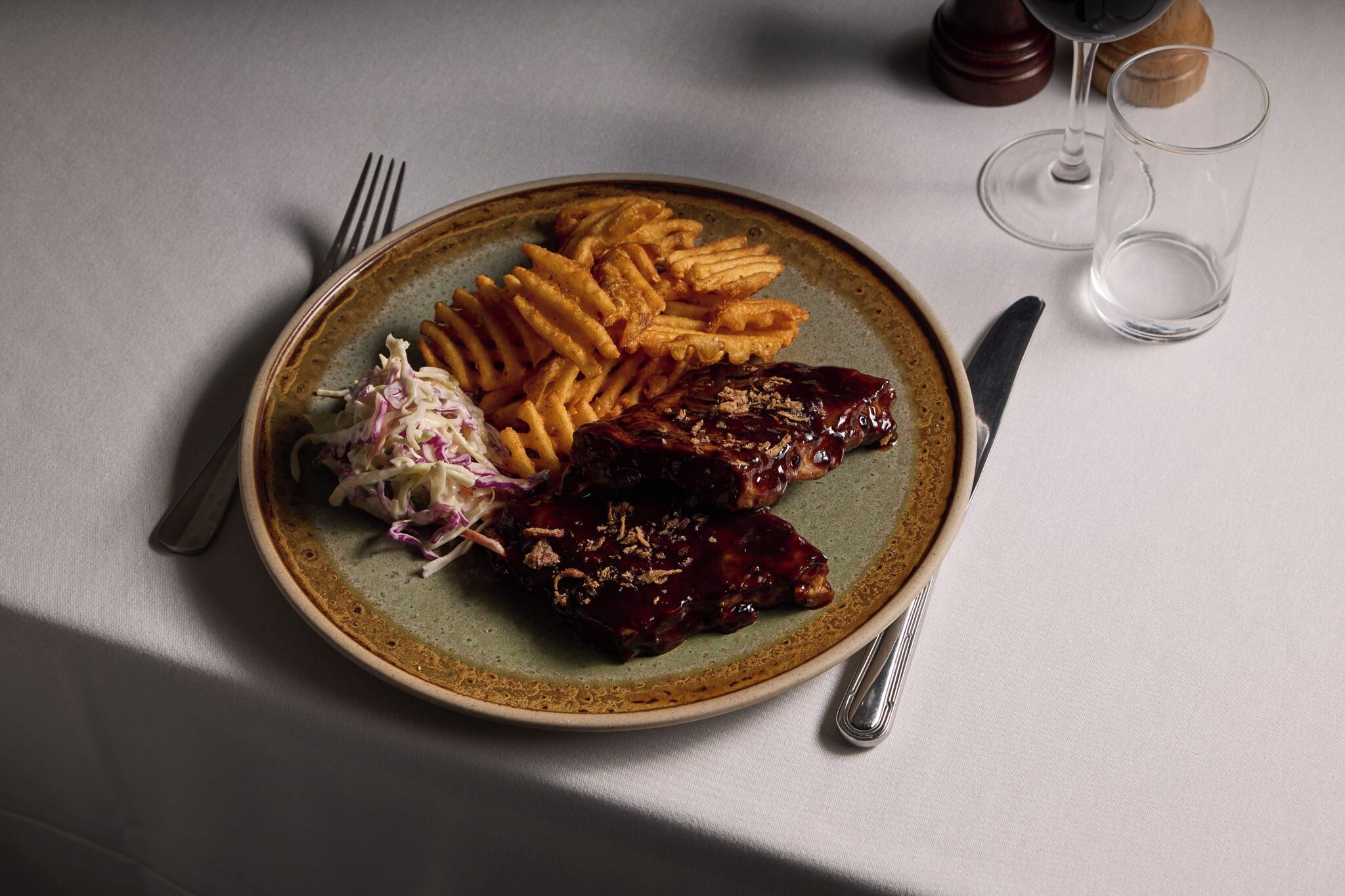 A plate of food with fries, coleslaw, and ribs on a ceramic plate.