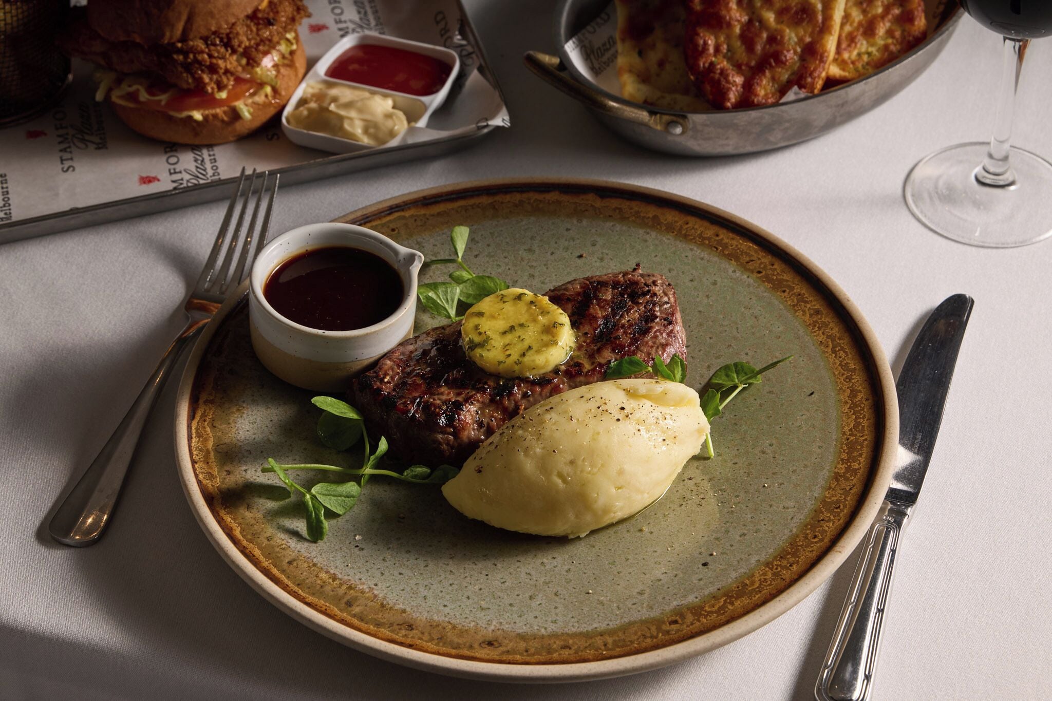 A plate with a steak, mashed potatoes, and a small bowl of sauce.