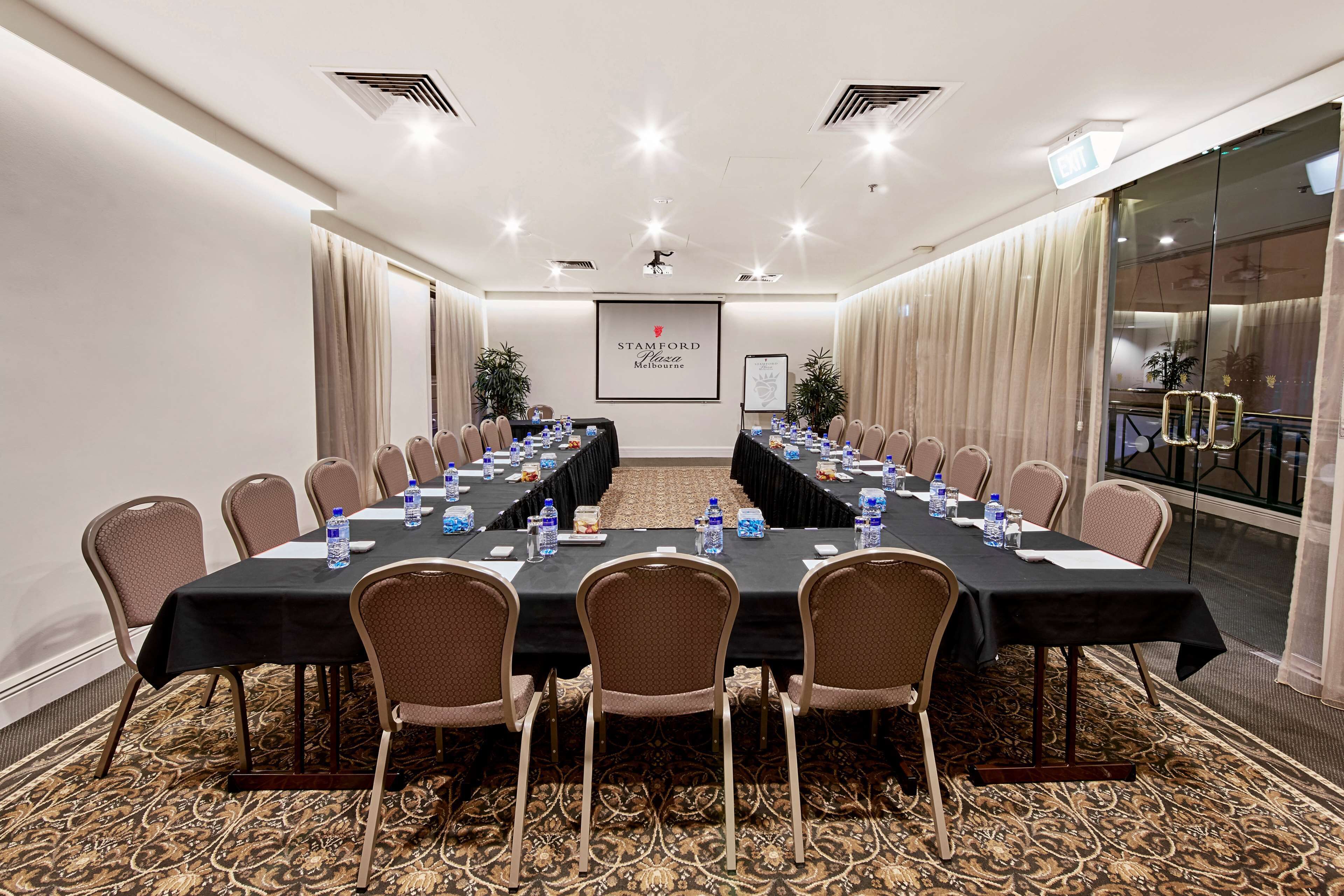 Un salón de conferencias con una larga mesa, sillas, botellas de agua y un cartel que dice 'STAMFORD Melbourne'.