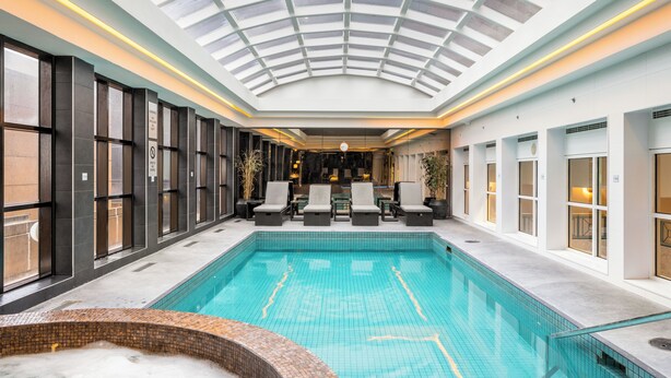 Una piscina interior moderna con techo de tragaluces, sillas de descanso y zona de hidromasaje.