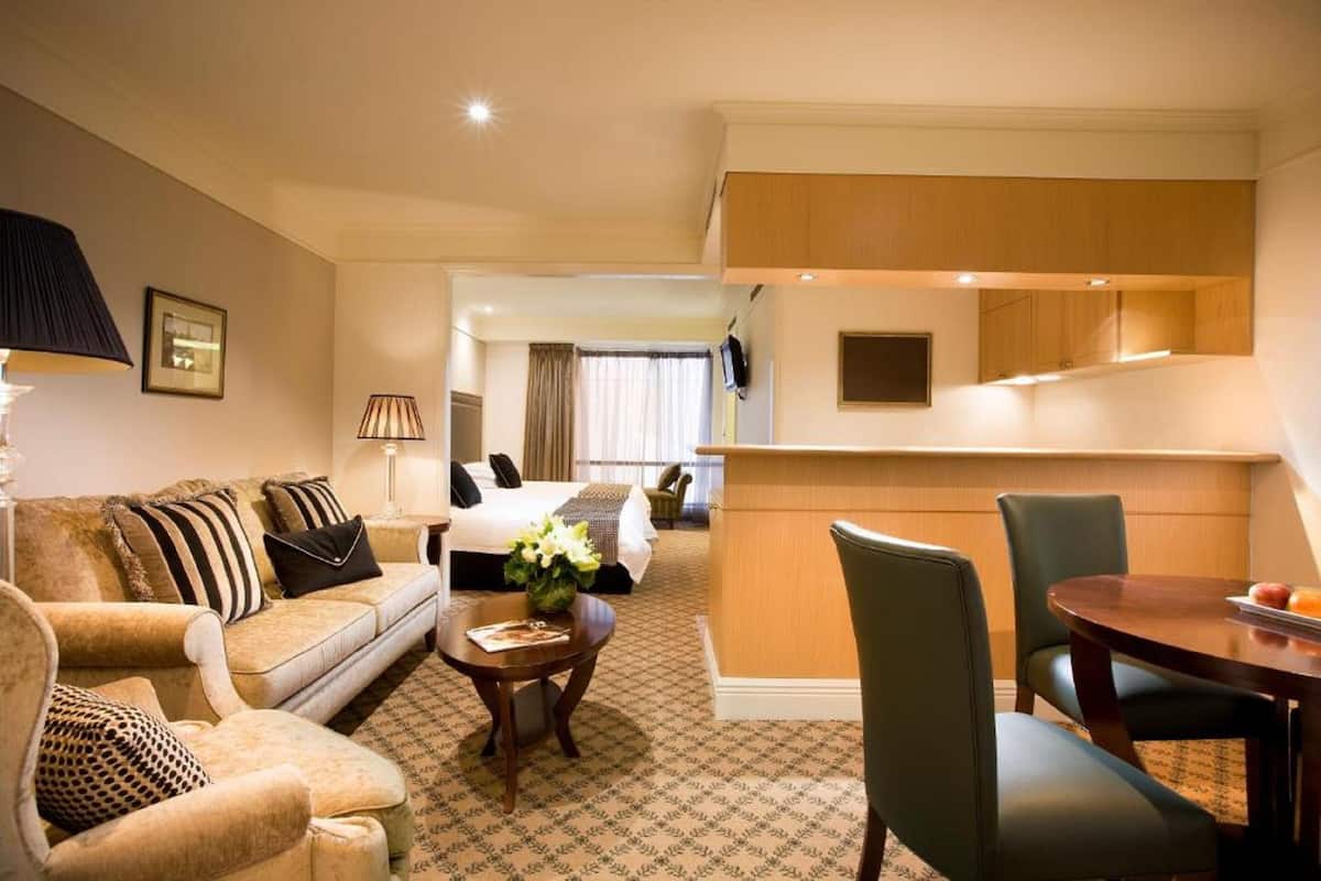 Une chambre d’hôtel comprenant un canapé, une petite table, une table à manger avec des chaises, un lit et un coin cuisine.