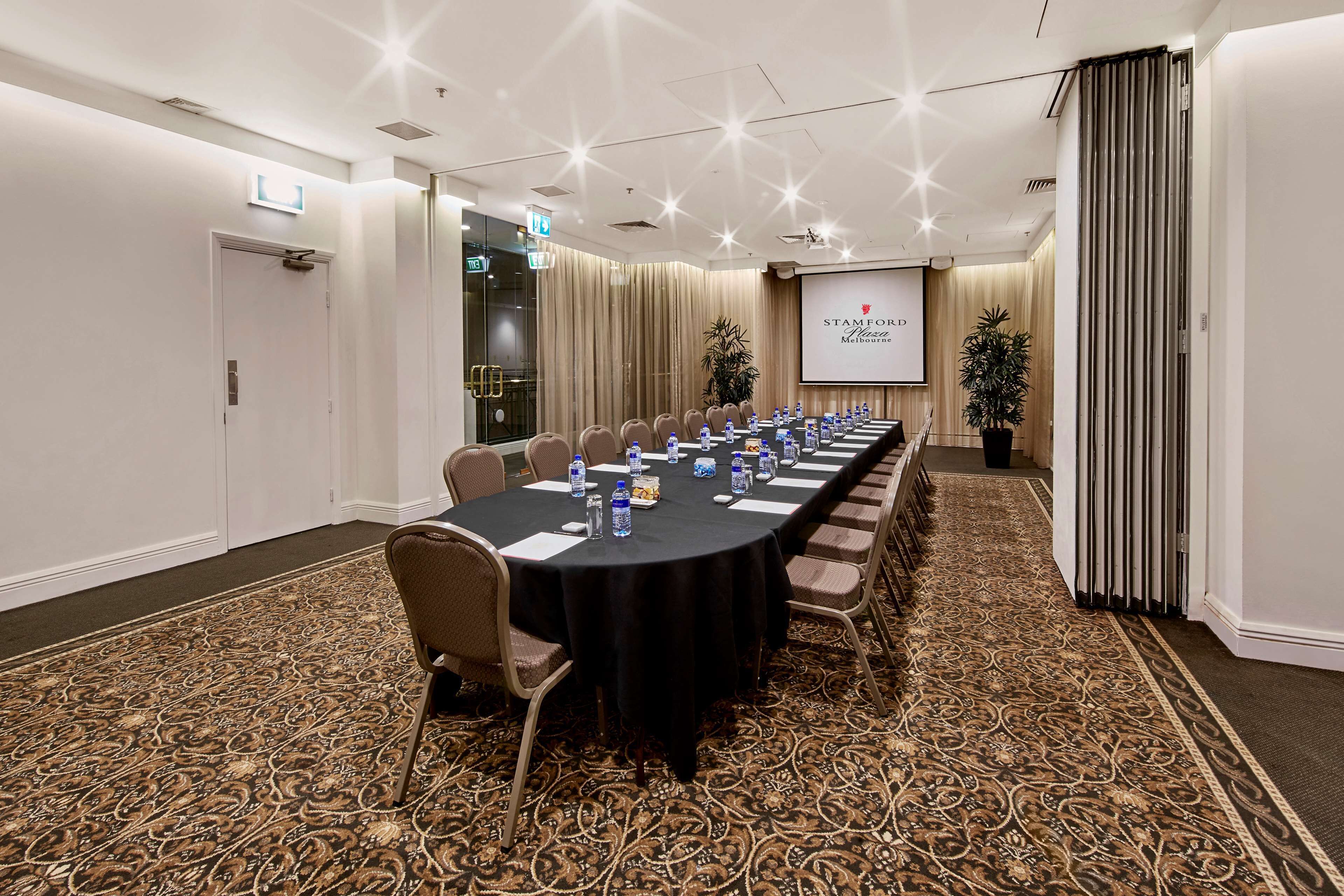 Een congrescentrum met een lange tafel, stoelen, een projectiescherm en een vloerbedekking.