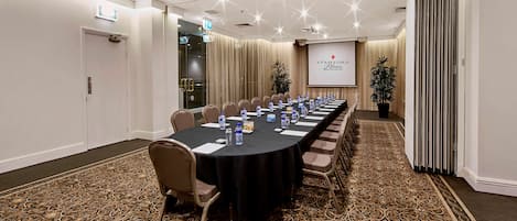 Een congrescentrum met een lange tafel, stoelen, een projectiescherm en een vloerbedekking.