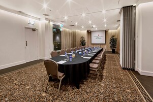 A conference room with a long table, chairs, a projector screen, and a carpeted floor.